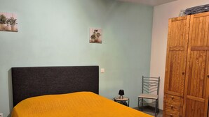 Makuuhuoneessa on sänky, vaatekaappi, tuoli, pieni pöytä ja seinälle kiinnitetty hylly, jossa on kasveja.