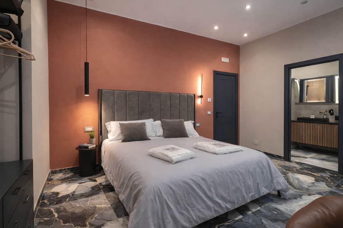 A modern hotel room with a large bed, marble flooring, a dark door, and a bathroom visible through an open doorway.