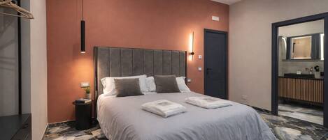 A modern hotel room with a large bed, marble flooring, a dark door, and a bathroom visible through an open doorway.