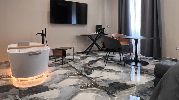 Quarto de hotel moderno com uma televisão de tela grande, uma pequena mesa com uma cadeira, uma banheira e piso de mármore.