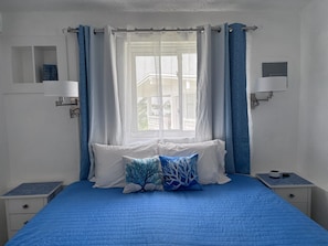 A bedroom with a bed, two bedside tables, a window with curtains, and wall-mounted lamps.