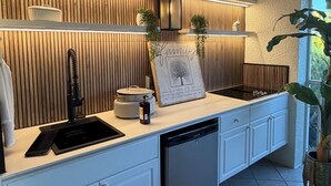 A modern kitchen with a built-in dishwasher, wooden paneling, and a framed family tree picture. - Perfect Snowbird Retreat – Sunny Condo Near Pool & Clubhouse (Naples)