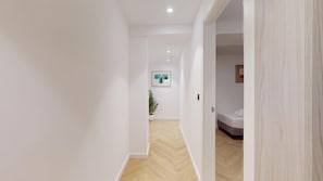 A hallway with a wooden floor, white walls, and a door leading to a bedroom with a bed and a bedside table. - MyFlats La Marina (Alicante)