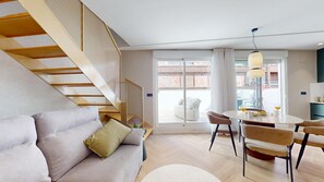A modern living room with a sofa, a dining table with chairs, a staircase, and a large window. - MyFlats La Marina (Alicante)