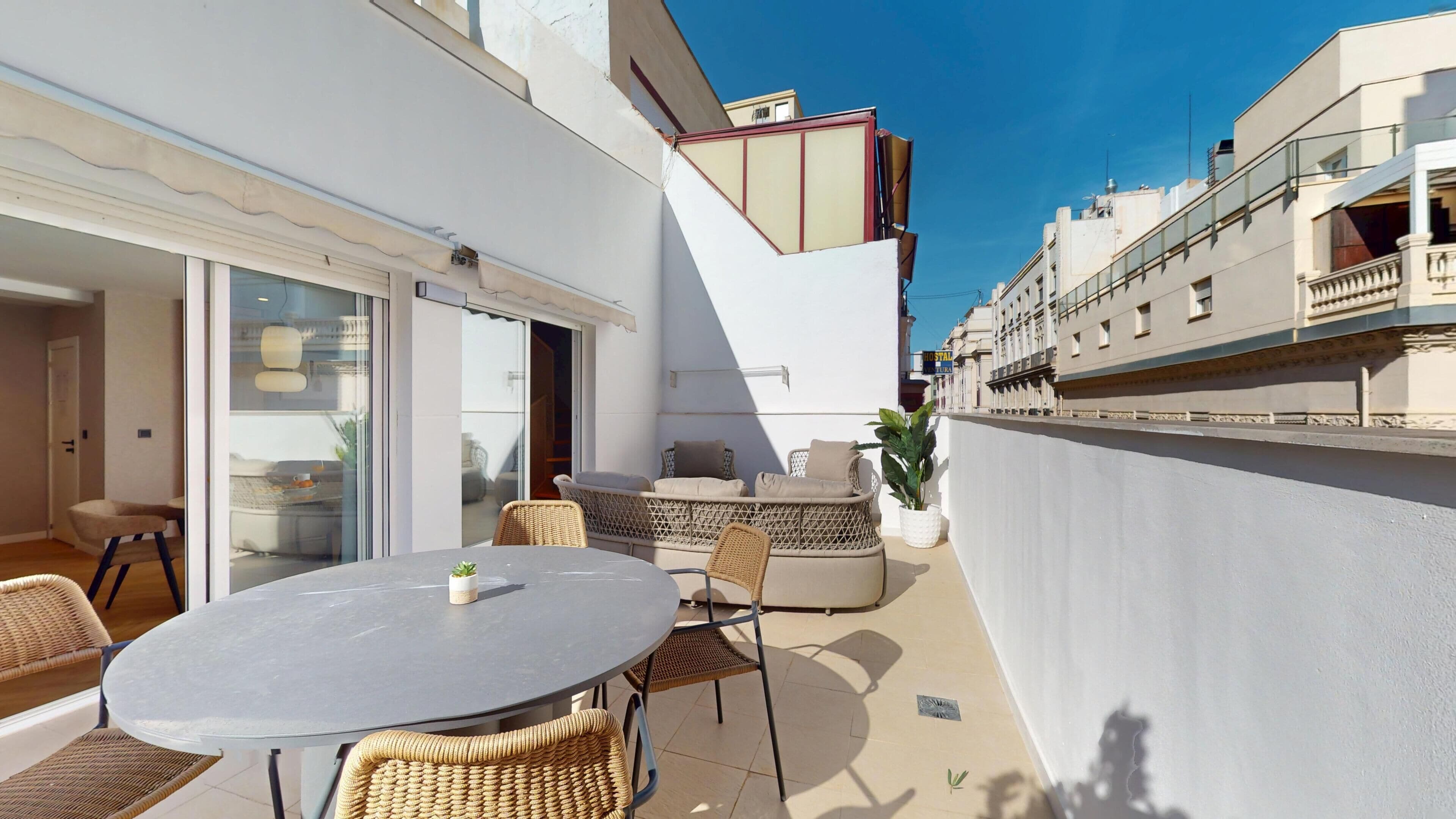 A patio with a round table and wicker chairs, a sliding glass door, and a white wall with a balcony.