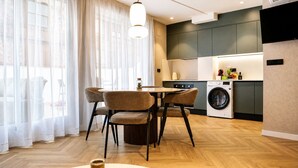 Een moderne keuken met een wasmachine, een eethoek met stoelen en een groot raam met transparante gordijnen.