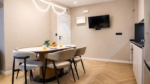 A modern kitchen with a flat-screen TV, a dining area with a wooden table and chairs, and a small plant on the table. - MyFlats La Marina (Alicante)