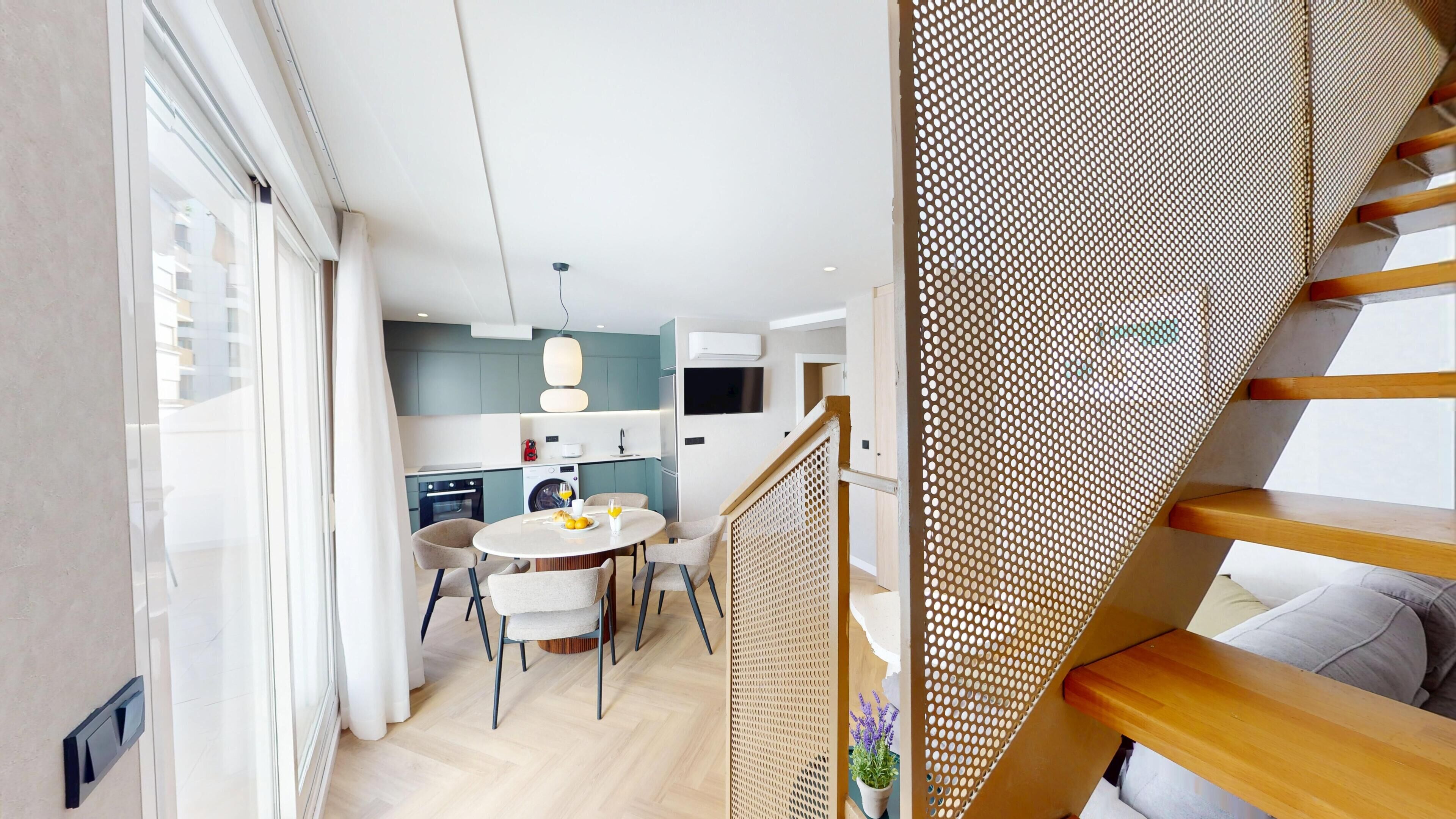 Una cocina moderna con comedor, una escalera de baranda de madera y vistas al exterior.