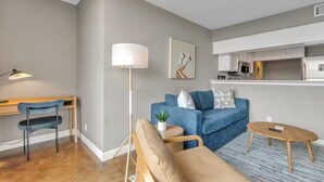 A modern living room with a blue sofa, a small round table, a desk with a chair, and a floor lamp. - Lively 2 BR Apt Downtown ATX (Austin)