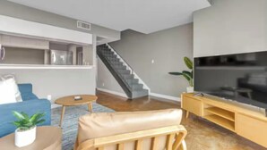 A modern living room with a sofa, coffee table, TV stand, and staircase. - Perfectly Located - Cool 2 BR Apt - Downtown ATX (Austin)