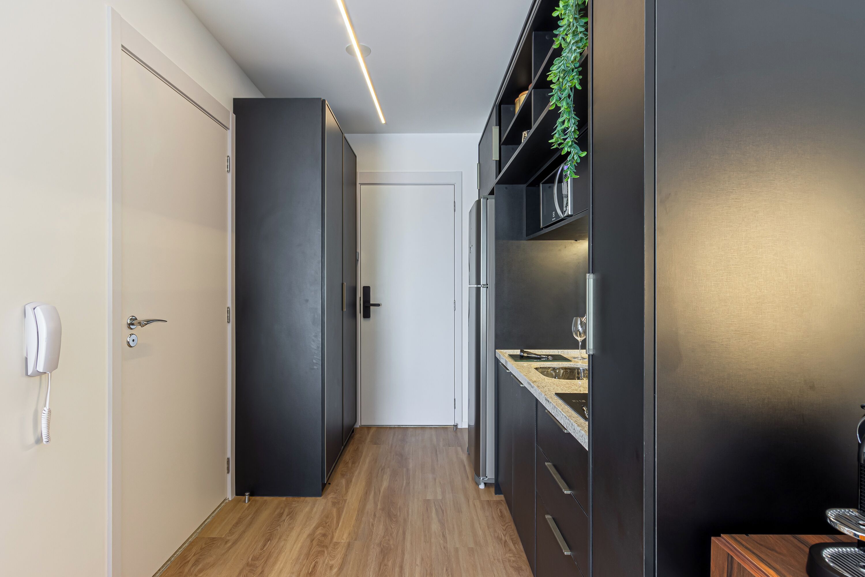 A narrow hallway with a wooden floor, a white door, and a black-framed mirror.