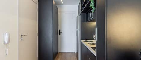 A narrow hallway with a wooden floor, a white door, and a black-framed mirror.