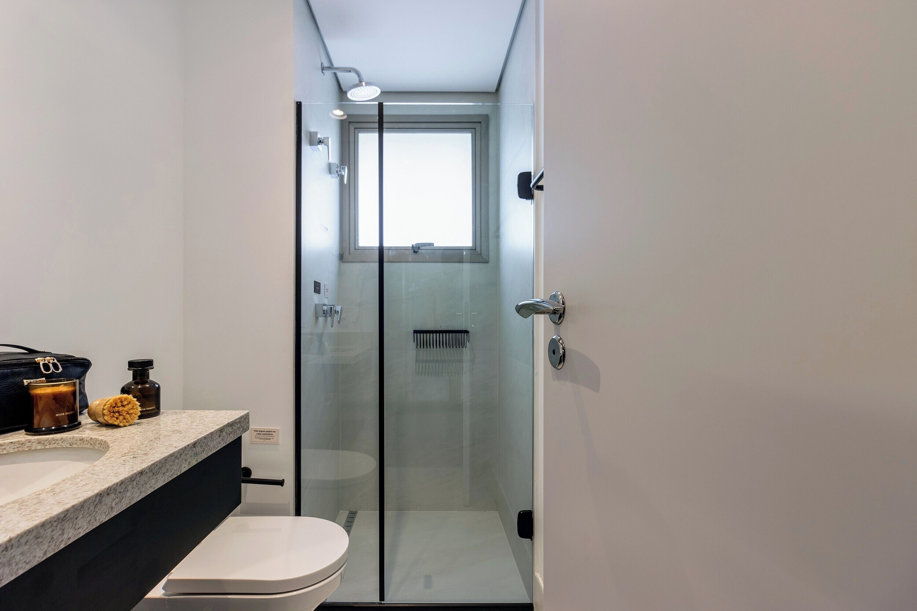 A modern bathroom with a glass-enclosed shower, a toilet, and a vanity with toiletries.