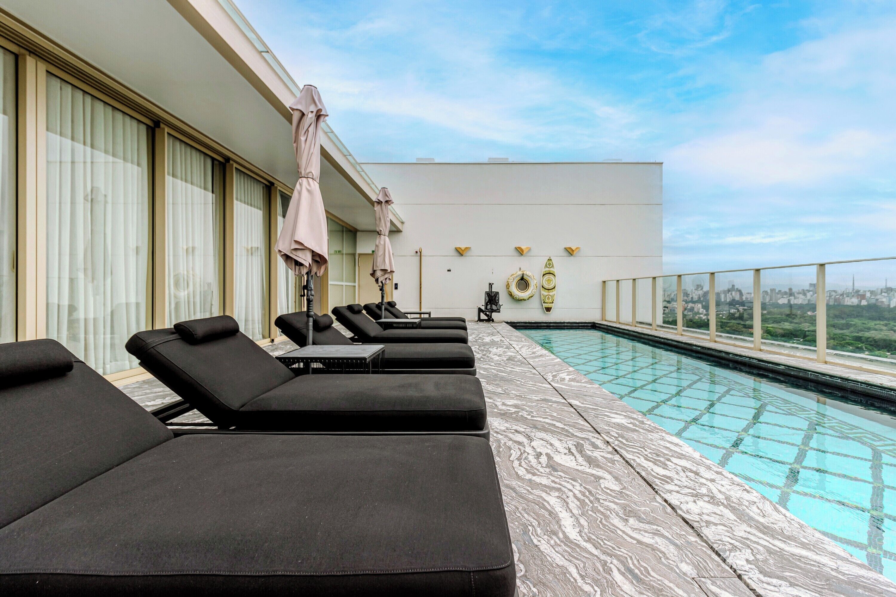 Un área de piscina en la azotea con sillones de descanso y sombrillas, piscina con vista despejada del paisaje urbano.