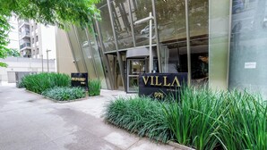 Moderni rakennus, jossa on lasijulkisivu, ja sen yläpuolella on kyltti, jossa lukee ”VILLA 591”. Lisäksi alueella on hyvin hoidettu puutarha, jossa kasvaa korkeaa ruohoa.