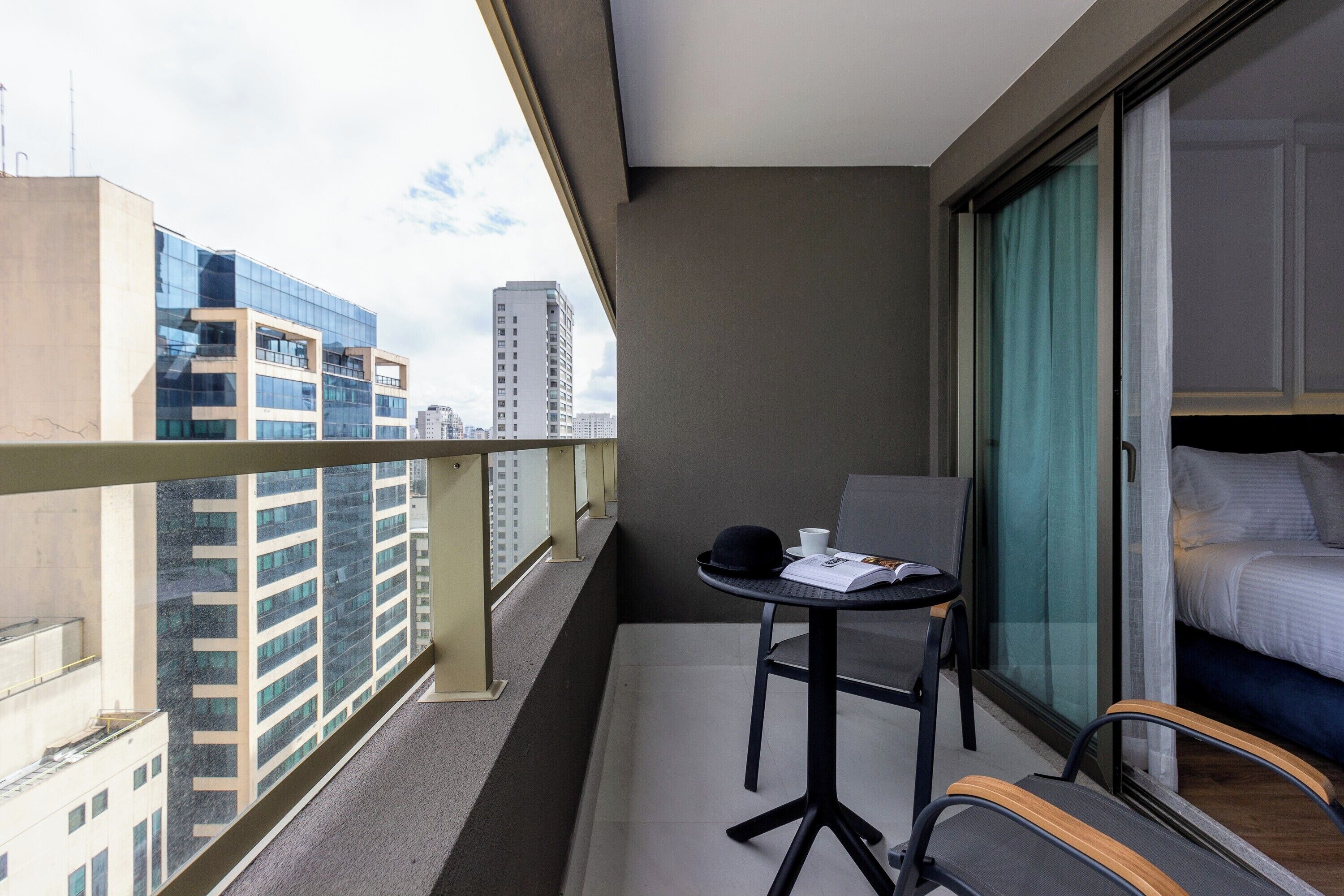 Un balcón con vistas a edificios de la ciudad, una mesa pequeña con una silla y una cama con cortina.