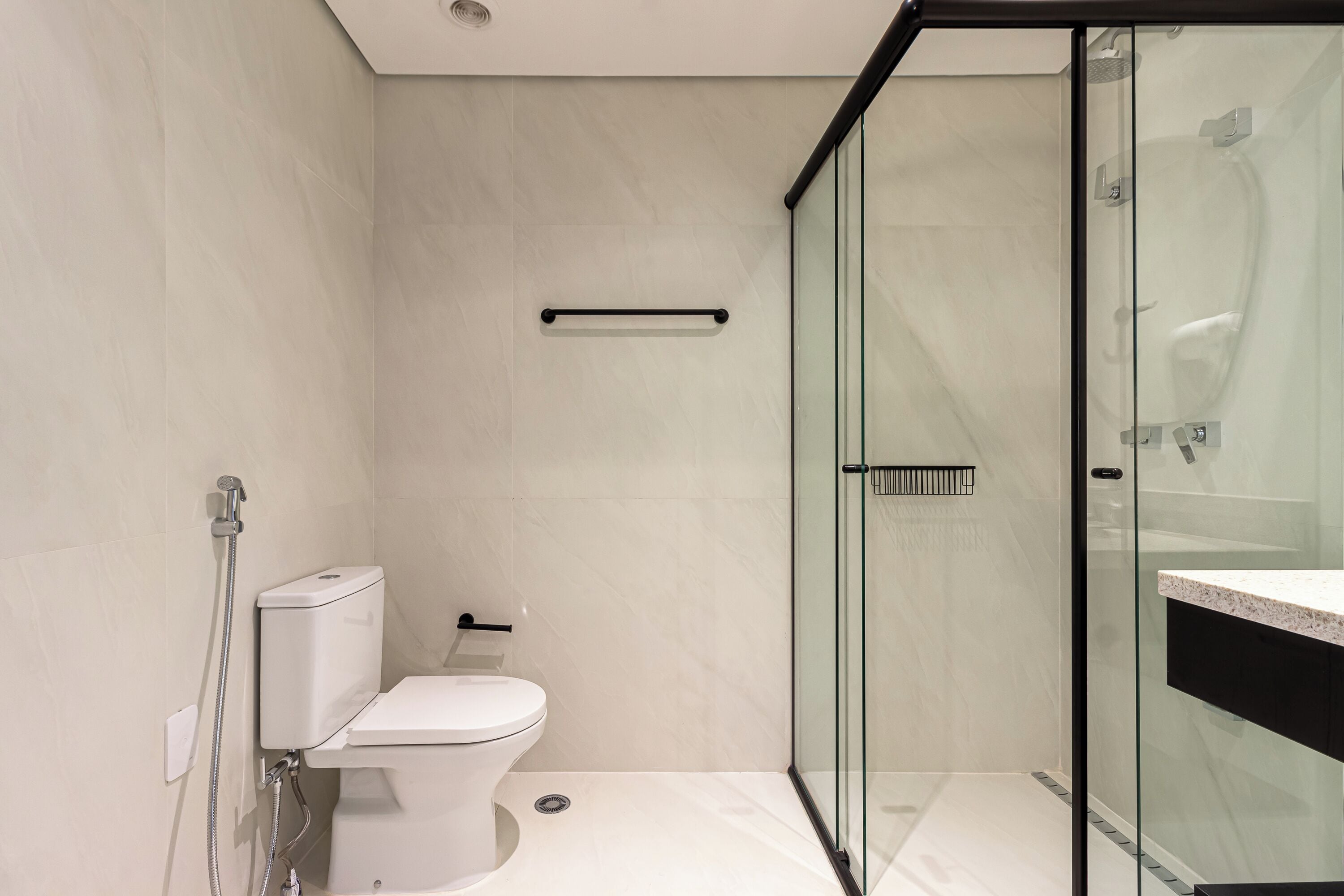 Een moderne badkamer met een douchecabine van glas, een toilet en een wastafel met een marmeren blad.