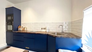 A kitchen with dark blue cabinets, a stainless steel sink, a toaster, and a kettle on the countertop.