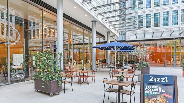 An outdoor dining area with tables and chairs, a large potted plant, and a menu stand for Zizzi. - Rathbone Exclusive - ES1 (London)