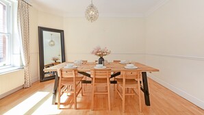 A dining room with a wooden table set for four, a vase of flowers, and a chandelier. - Rathbone Exclusive - ES1 (London)