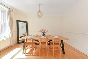 Ein Esszimmer mit einem Holztisch, gedeckt für vier Personen, einer Blumenvase und einem Kronleuchter.