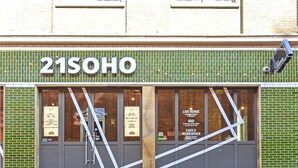 A storefront with a green tiled facade, large windows, and a sign reading '21SOHO'. - Rathbone Exclusive - ES1 (London)