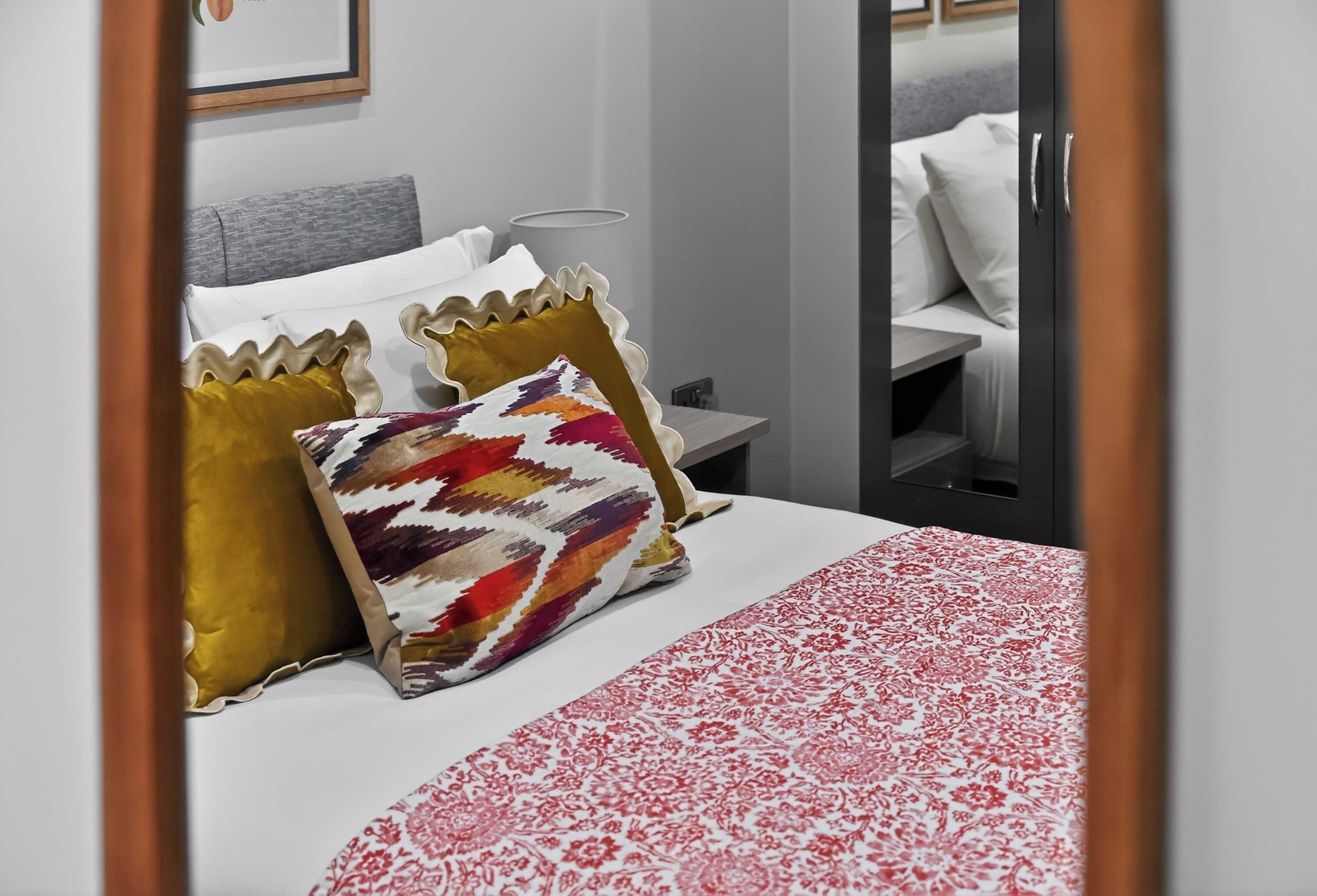 A hotel room with a bed, a nightstand, and a mirror.