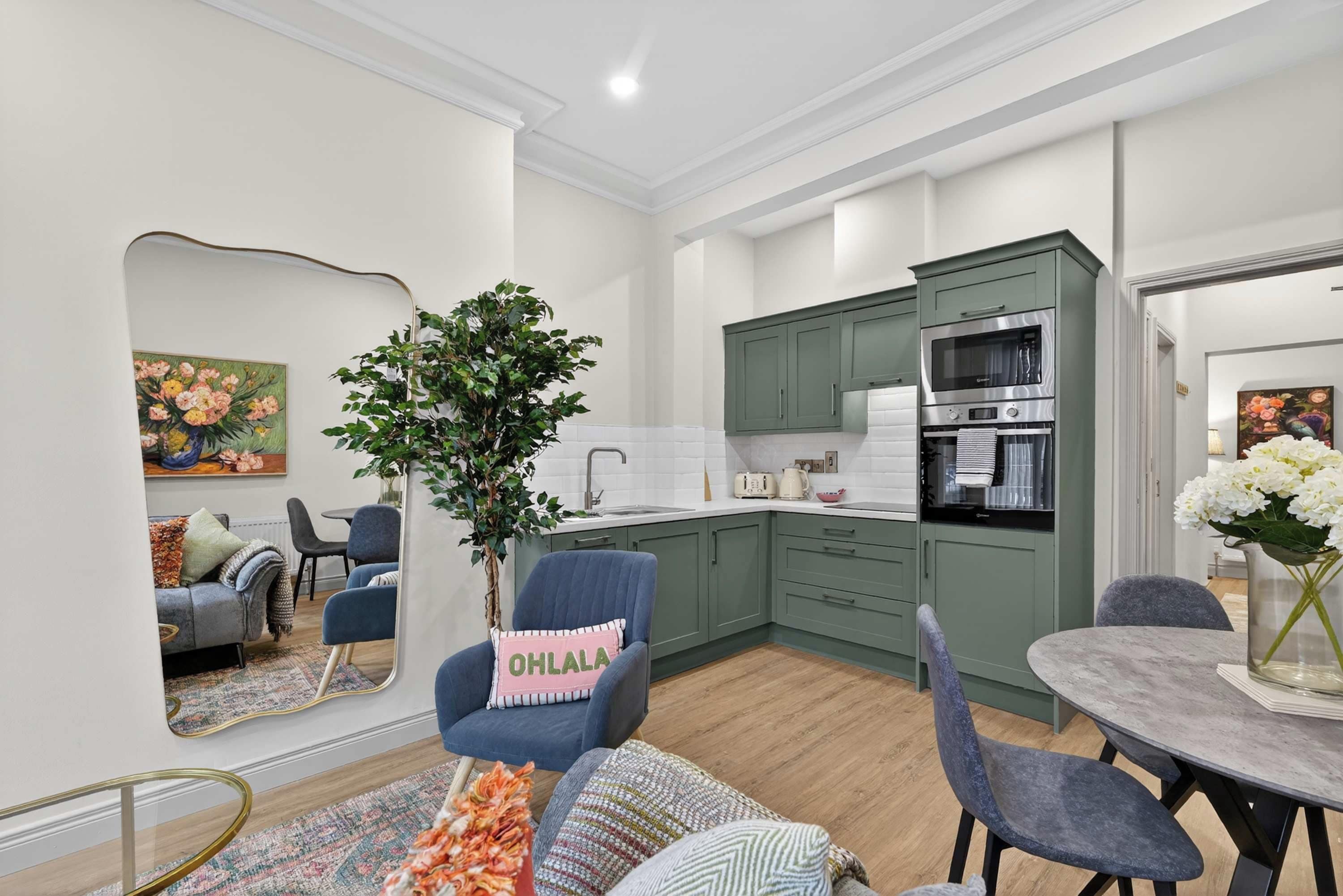 Une cuisine moderne avec des meubles de couleur verte, un four encastré et un coin repas comprenant une table ronde et des chaises.