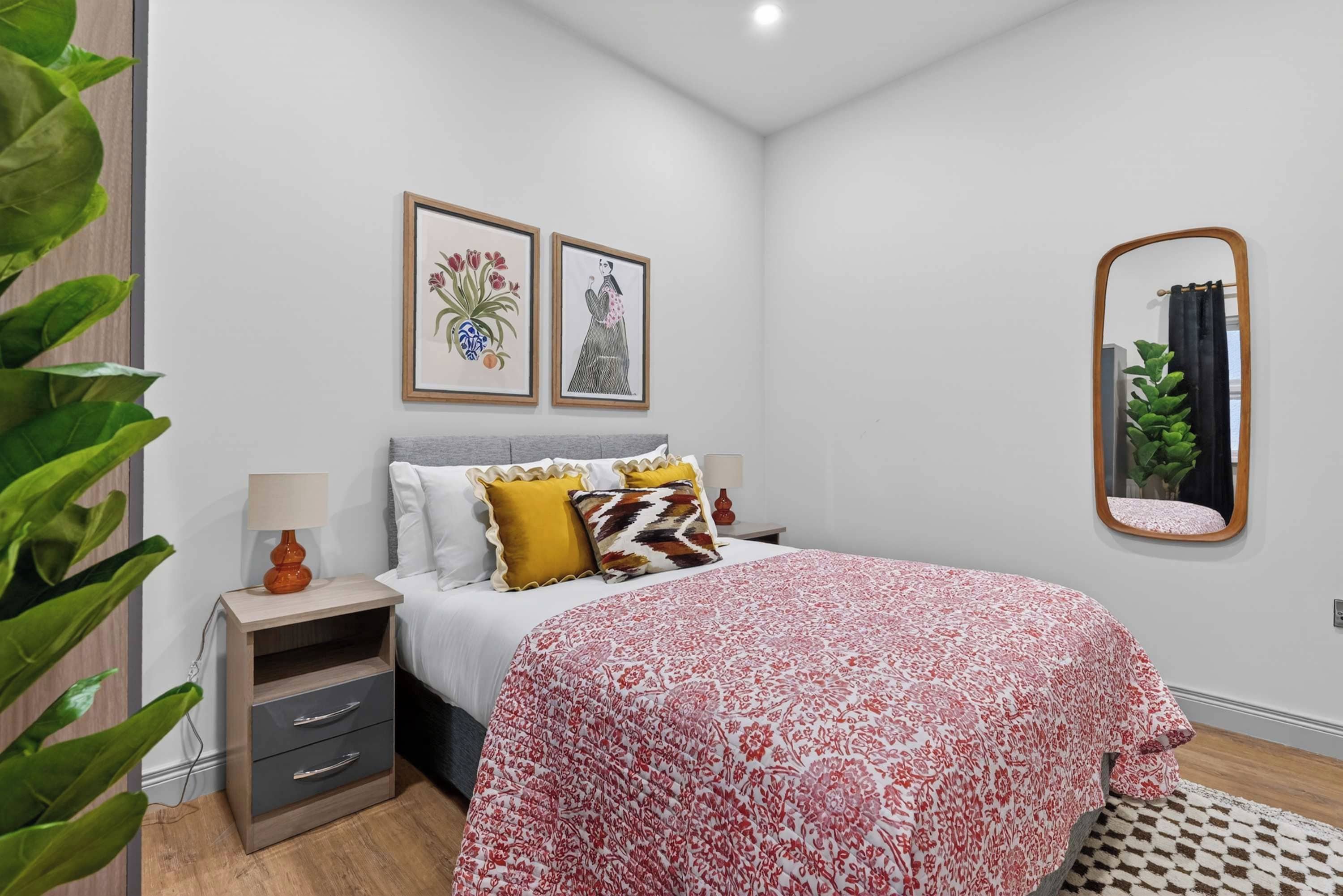 A bedroom with a bed, bedside tables, a mirror, and framed artwork on the wall.