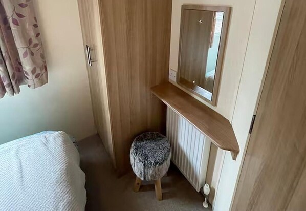 Une petite pièce, de taille modeste, comprenant une armoire en bois, un petit tabouret, un miroir et un radiateur.