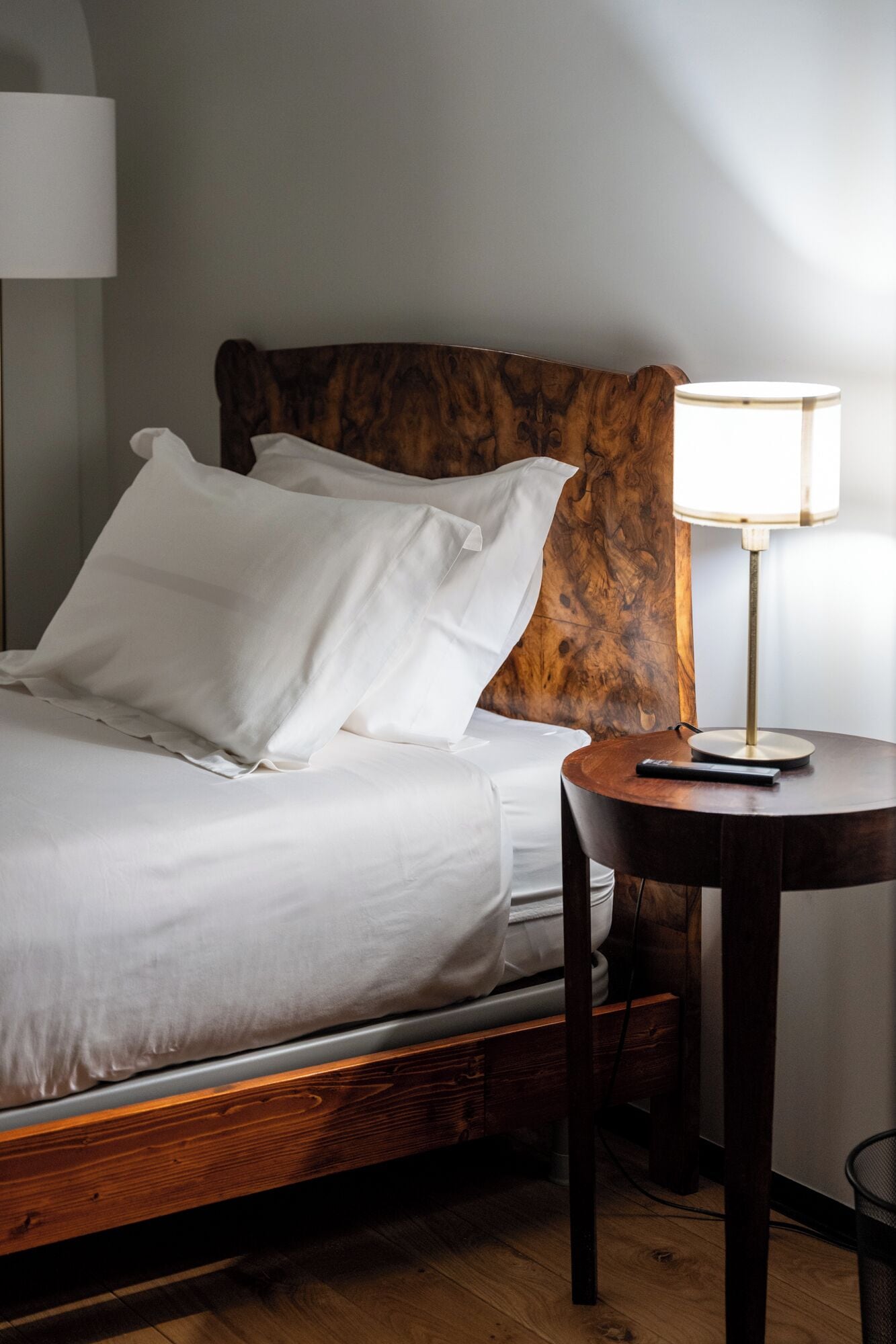A neatly made bed with white linens, a wooden headboard, and a bedside table with a lamp.