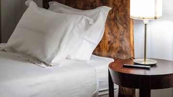 A neatly made bed with white linens, a wooden headboard, and a bedside table with a lamp.