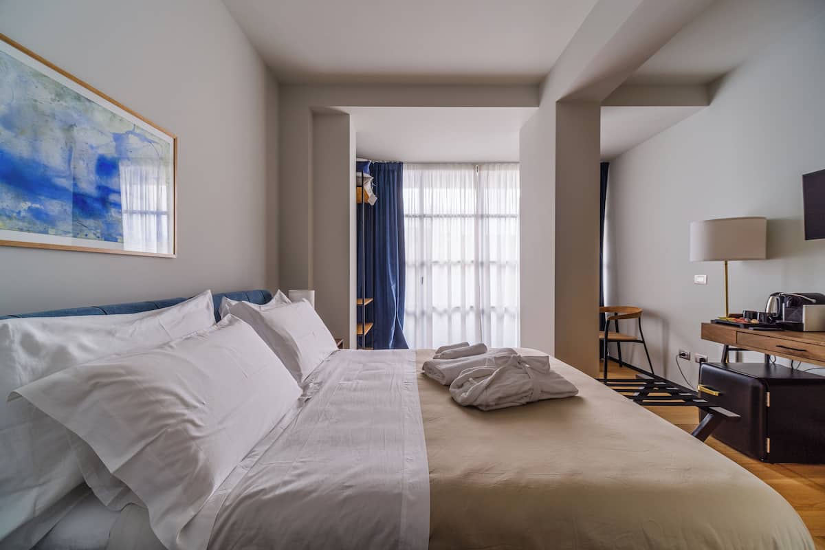 A hotel room with a bed, a desk, a chair, a TV, and a window with curtains.