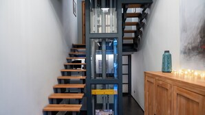 A modern staircase with wooden steps and metal railings, leading to a room with a wooden cabinet and a decorative vase. - Club64  (Andria)