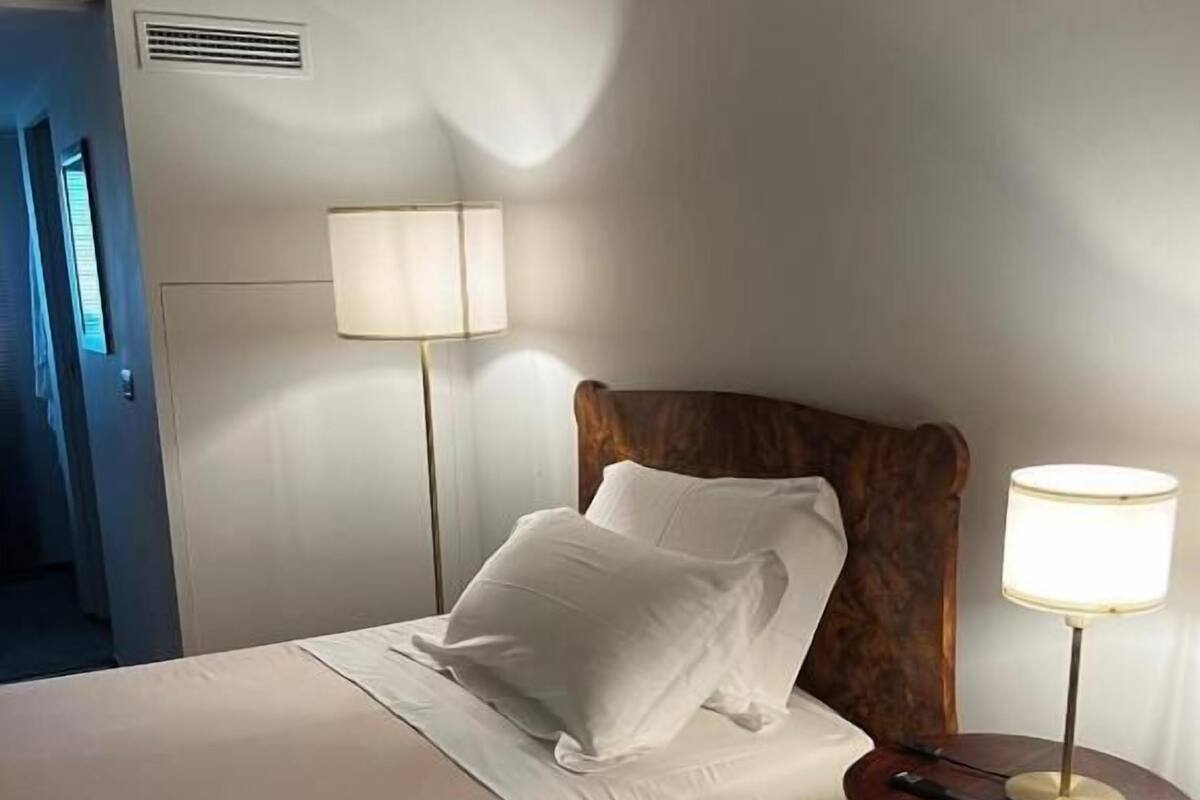 A hotel room with a bed, two bedside lamps, a round table with a lamp, and a door.