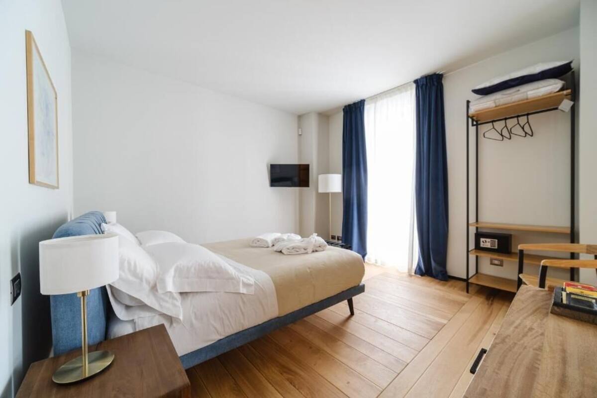 A hotel room with a bed, bedside table, lamp, TV, and a wooden desk.