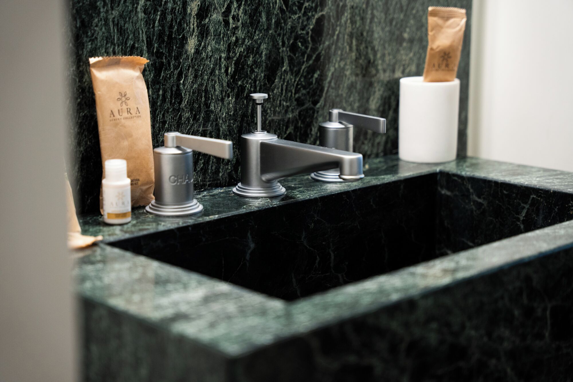 A bathroom with a black marble sink, two faucets, and a bottle of hand soap.
