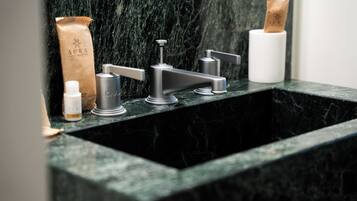 A bathroom with a black marble sink, two faucets, and a bottle of hand soap.