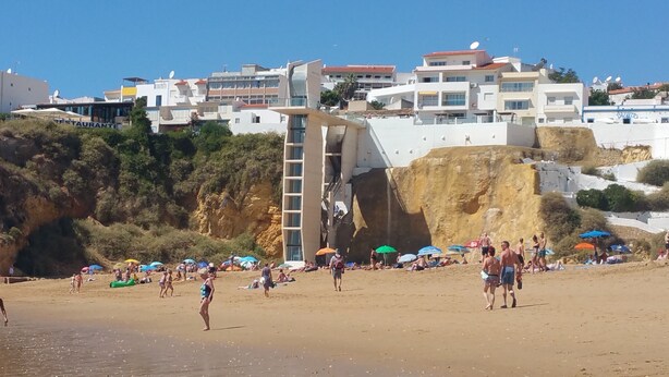 A beach with people sunbathing and walking. There are umbrellas and a building with a unique design in the background. - Sea and Sun Set view (Albufeira)