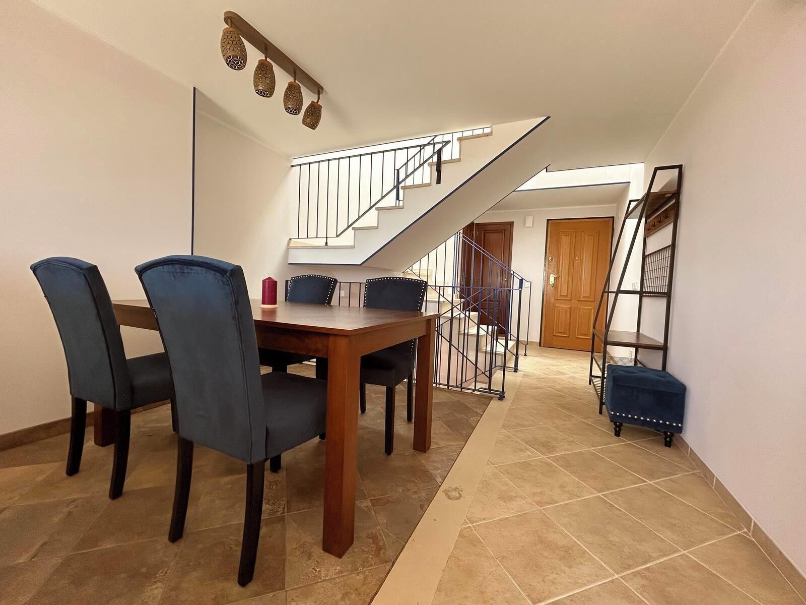 A dining area with a wooden table and chairs, a staircase, and a door.