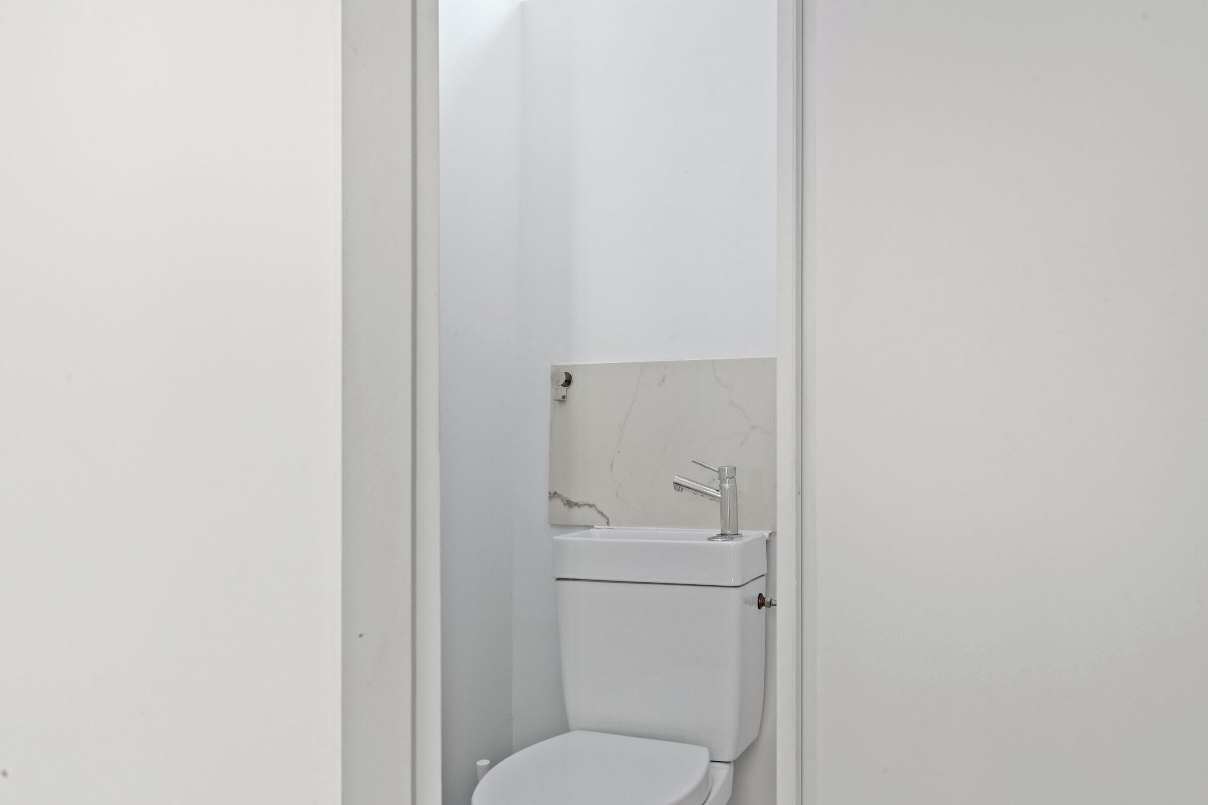 A small, white bathroom with a toilet, a sink, and a marble backsplash.