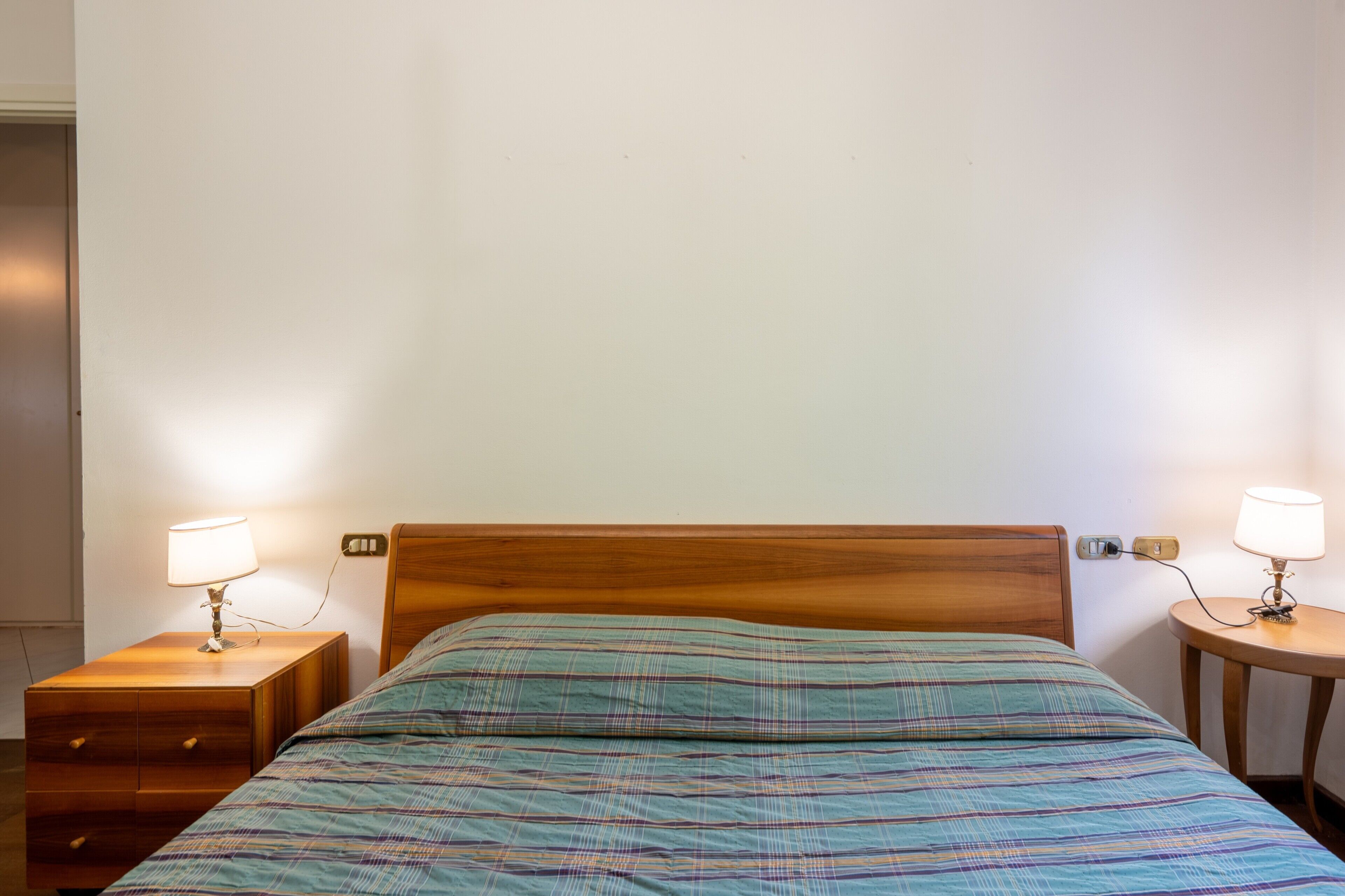 A bed with a wooden headboard, two bedside tables with lamps, and a wall socket.