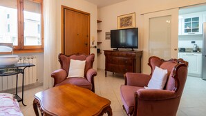 A living room with a wooden table, two armchairs, a television, and a door leading to a kitchen. - Apartment 'Casa Levanella' with Private Garden (Montevarchi)