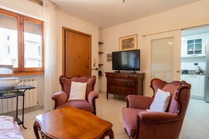 Ein Wohnzimmer mit einem Holztisch, zwei Sesseln, einem Fernseher und einer Tür zu einer Küche.