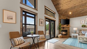 Un salon chaleureux avec une cheminée, un plancher en bois et un coin salon confortable avec des fauteuils et une table.