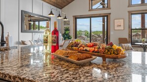Un comptoir de cuisine avec un plateau de fruits, des bouteilles de vin et un panier à pain.