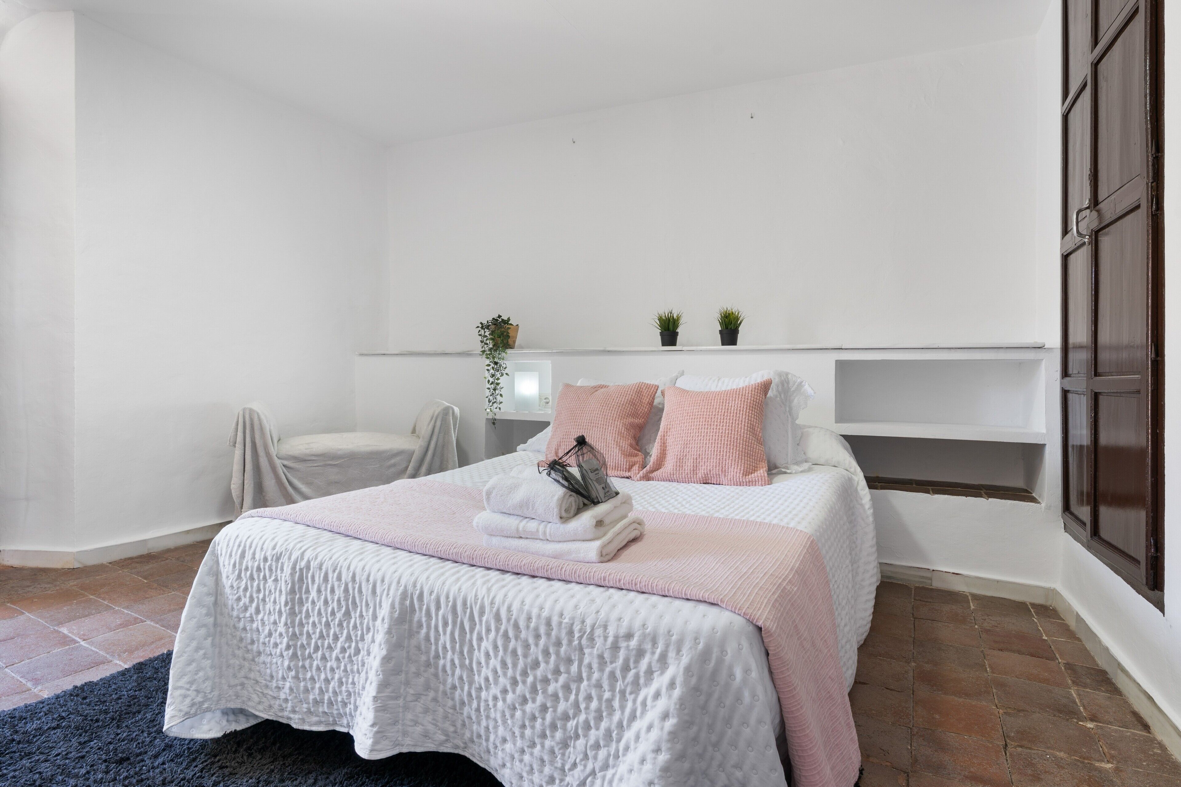 Een slaapkamer met een bed, nachtkastje, plantenplank en een raam.