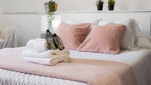 Un lit bien fait, avec une literie rose et blanche, une serviette blanche pliée et une paire de chaussures posées sur le lit.