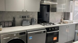 A modern kitchen with grey cabinets, a built-in stove, a dishwasher, and a coffee maker. - House Sleeps 6 With Garden and Parking (Leeds)