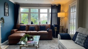A living room with a brown leather sofa, a glass coffee table, a grey sofa, and a floor lamp. - House Sleeps 6 With Garden and Parking (Leeds)